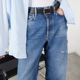 Model wearing Acne 1981 U Vintage Wide-Leg Jeans in mid blue with whiskering detail, styled with a black belt and blue striped shirt.