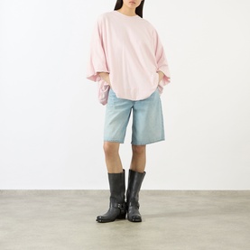 Model wearing Acne white oversized T-shirt with ruched sleeves, styled with light blue denim shorts and black knee-high boots.