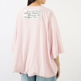 Model wearing Acne white oversized cotton-hemp T-shirt, rear view showing branded label graphic, styled with light blue jeans.