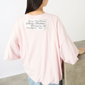 Model wearing Acne white oversized T-shirt, back view showing cursive logo graphic print, drop shoulders, relaxed fit