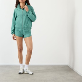 Model wearing Adanola Shorts in Eucalyptus Green, styled with matching zip-up jacket and white trainers.