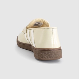Cream patent leather low-top trainer, rear view, white side stripe detail and brown gum rubber sole.