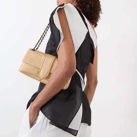 Model carrying Jacquemus Le Bambino Chaine Shoulder Bag in Natural woven leather with gold chain strap, styled with monochrome top and white trousers
