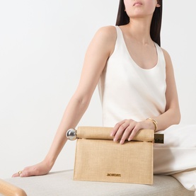 Model carrying Jacquemus La Pochette Rond Carr&eacute; Clutch in natural woven finish with silver-tone circular handle, styled with white vest top.