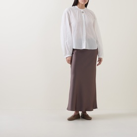 Model wearing Luisa Cerano off white cotton-silk shirt with gathered neckline and balloon sleeves, styled with brown satin midi skirt and taupe flats.