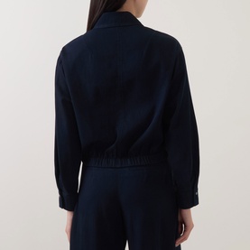 Model wearing Luisa Cerano Blouson Denim Blouse in dark blue, back view, elasticated hem, long sleeves with buttoned cuffs, styled with matching