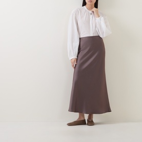 Model wearing Luisa Cerano olive satin midi skirt with white tie-neck blouse and flat mules.