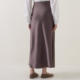 Model wearing Luisa Cerano olive satin midi skirt, rear view, styled with a white long-sleeve blouse and flat mules.
