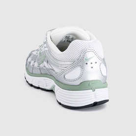 Nike trainer in metallic silver and white, shown from rear angle with chunky white sole and sage green heel tab detail.