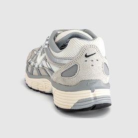 Nike trainer in light bone and sail, rear three-quarter view showing grey suede overlays, white midsole and black Swoosh logo