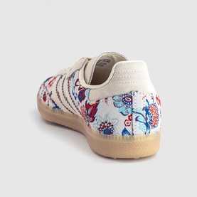 Adidas trainer in Liberty off white with floral print upper, three-stripe detail, and gum sole, shown from rear angle.