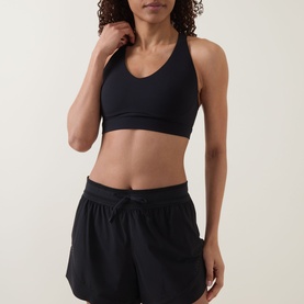 Model wearing black sports bra with V-neck and racerback design, styled with black drawstring shorts
