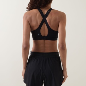 Model wearing black sports bra with cross-back strap detail, paired with black shorts, rear view