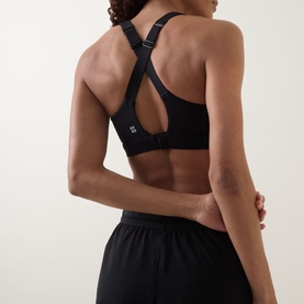 Model wearing black sports bra with racerback cross-strap detail and keyhole cutout, paired with black shorts