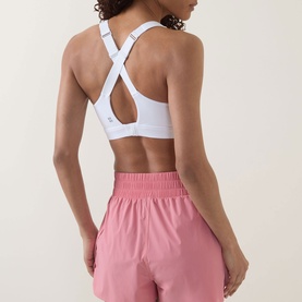 Model wearing Sweaty Betty sports bra in Dove White with cross-back straps, styled with pink shorts, rear view.