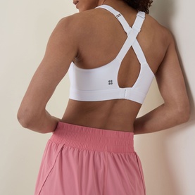 Model wearing Sweaty Betty sports bra in Dove White with crossback straps, styled with pink wide-leg shorts