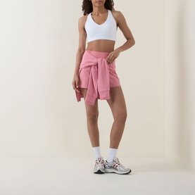 Model wearing Sweaty Betty Dove White sports bra with pink shorts and tied sweatshirt at waist, styled with white socks and trainers
