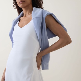 Model wearing Sweaty Betty white dress with light blue hoodie tied over shoulders, cropped torso view