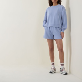 Model wearing Sweaty Betty Laguna Blue hoodie styled with matching shorts and white trainers