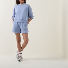 Model wearing Sweaty Betty Laguna Blue sweatshirt with matching shorts and white chunky trainers.