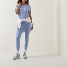 Model wearing Sweaty Betty Laguna Blue Marl leggings and matching tee, styled with white tied jacket and grey trainers.