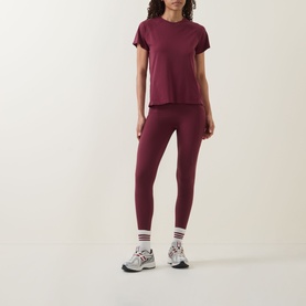 Model wearing Sweaty Betty Merlot Red leggings with matching T-shirt and white chunky trainers with stripe socks.