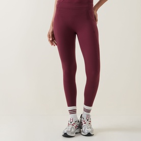 Model wearing Sweaty Betty Merlot Red leggings, styled with white ankle socks and chunky grey trainers.