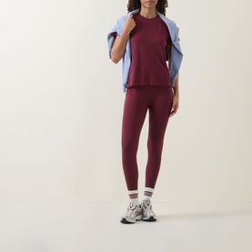 Model wearing Sweaty Betty Merlot Red leggings with matching top, light blue jacket draped over shoulder, white sports socks and trainers