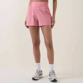 Model wearing Sweaty Betty melrose pink high-waisted shorts, styled with white sports socks and grey trainers.