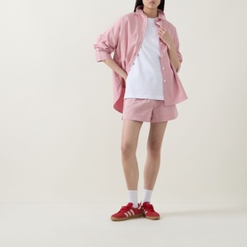 Model wearing Sweaty Betty Pink White Stripe shorts, styled with matching oversized shirt, white tee, socks and red trainers.