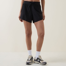 Model wearing black loose-fit running shorts with elasticated waist, styled with white ankle socks and grey trainers