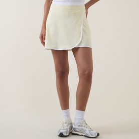 Model wearing Sweaty Betty Tennis Skort in Yellow/White, styled with white ankle socks and grey chunky trainers.