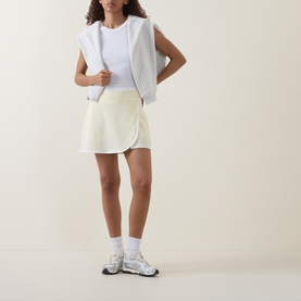 Model wearing Sweaty Betty Tennis Skort in Yellow/White, styled with a white vest top, ankle socks and grey trainers.