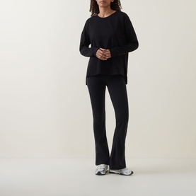 Model wearing Sweaty Betty After Class Open Back Tie Sweatshirt in black, styled with matching black flared trousers and silver trainers.