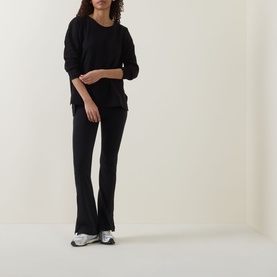 Model wearing Sweaty Betty After Class Open Back Tie Sweatshirt in black, styled with matching black flared trousers and silver trainers.