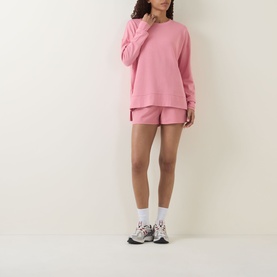 Model wearing pink oversized crew neck sweatshirt with matching pink shorts, styled with white ankle socks and chunky trainers