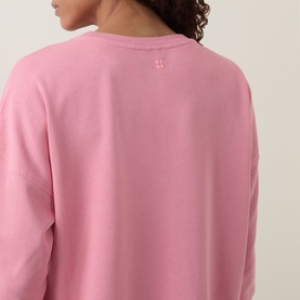 Model wearing a pink long-sleeve sweatshirt, rear view showing relaxed fit and small logo detail at back neck