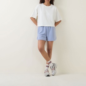 Model wearing Sweaty Betty Dove White oversized crop sweat tee with light blue shorts, striped socks and chunky trainers