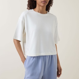 Model wearing Sweaty Betty Dove White cropped sweat top with short sleeves, styled with light blue wide-leg trousers