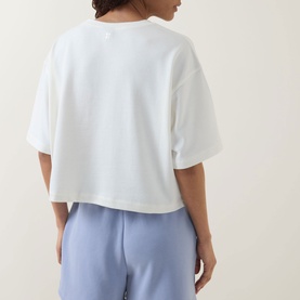 Model wearing Sweaty Betty Dove White cropped sweatshirt, styled with light blue wide-leg trousers, rear view.