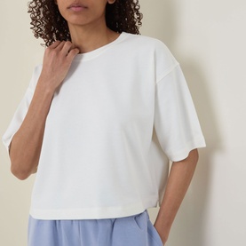 Model wearing Sweaty Betty Dove White oversized cropped sweat tee, styled with light blue shorts