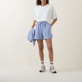 Model wearing Sweaty Betty shorts in Dove White, styled with a white oversized tee, white socks and chunky trainers, holding a matching hoodie