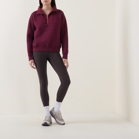 Model wearing Sweaty Betty Wind Down Textured Half-Zip Sweatshirt in Merlot Red, styled with dark leggings and grey trainers.