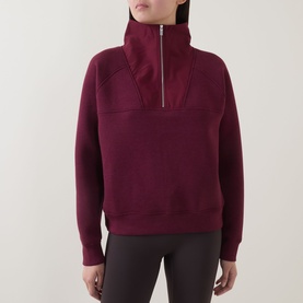 Model wearing Sweaty Betty Wind Down Textured Half-Zip Sweatshirt in Merlot Red with silver zip detail, styled with dark leggings.