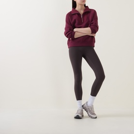 Model wearing Sweaty Betty Wind Down Textured Half-Zip Sweatshirt in Merlot Red, styled with dark leggings and grey trainers.