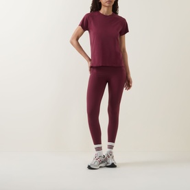 Model wearing Sweaty Betty Merlot Red T-shirt with matching leggings, white stripe socks and chunky trainers.