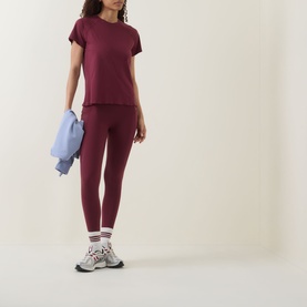 Model wearing Sweaty Betty Merlot Red T-shirt with matching leggings, styled with white trainers and carrying a light blue jacket.