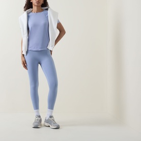 Model wearing Sweaty Betty Laguna Blue T-shirt, styled with matching leggings, white vest and grey trainers