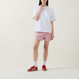 Model wearing Sweaty Betty Holiday Graphic T-Shirt in Red Equipment Print, styled with pink oversized shirt, pink shorts, and red Adidas trainers.