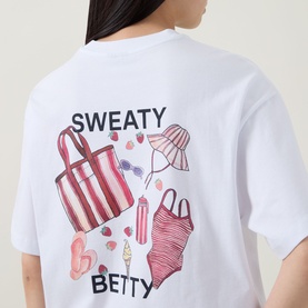 Model wearing Sweaty Betty Holiday Graphic T-Shirt in Red Equipment Print, styled under a pink stripe overshirt, close-up crop view.
